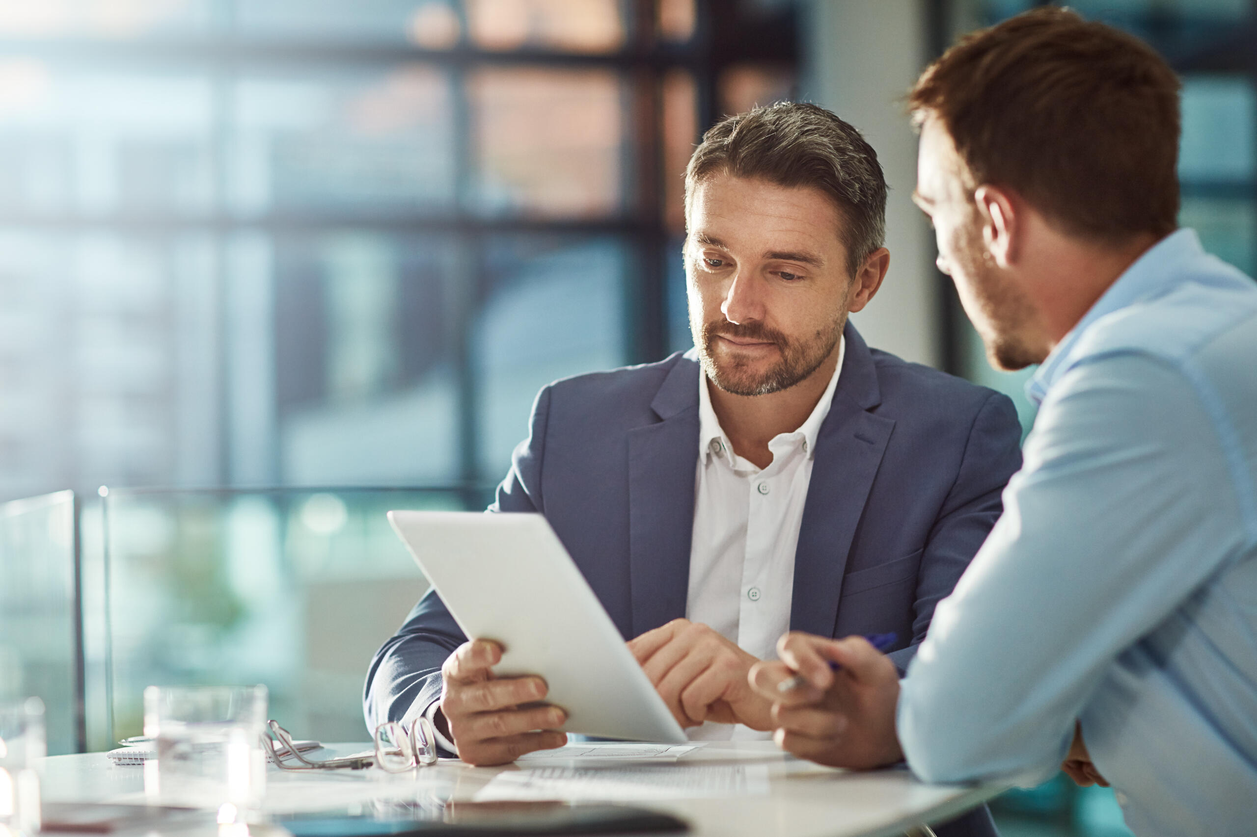 Picture of man sitting with colleague holding a tablet.